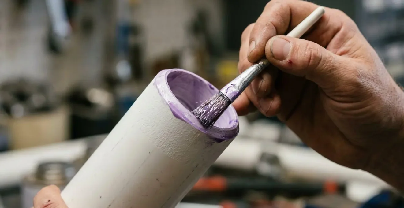 Gros plan sur les mains d'un plombier appliquant de la colle PVC sur un raccord avec un pinceau